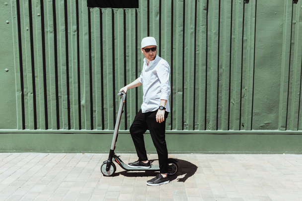 Modern man dressed white shirt and black pants standing at the street with electric scooter - Valokuva, kuva
