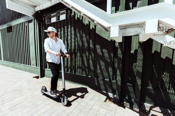 Modern man dressed white shirt and black pants standing at the street with electric scooter - Foto, afbeelding
