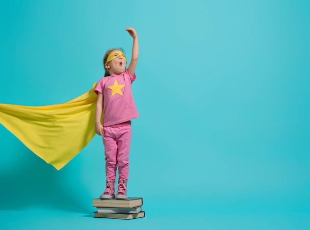 Little child playing superhero. Kid on the background of bright blue wall. Girl power concept. Yellow, pink and  turquoise colors.                              - Photo, image