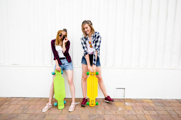 Two cheerful funny girl wearing checkered shirts posing against street wall at the street - 写真・画像