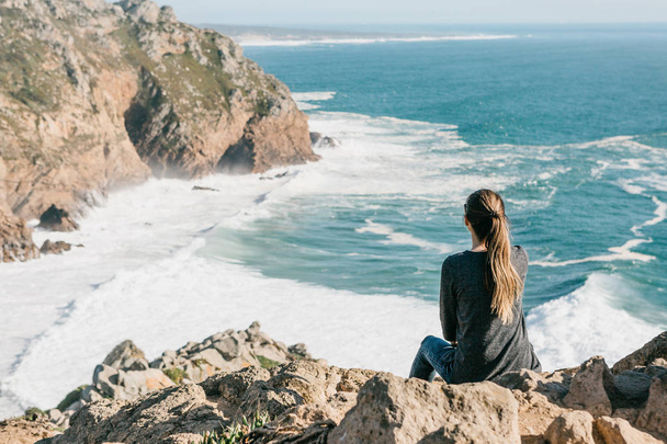 Το κορίτσι στην κορυφή του βράχου στη μοναξιά θαυμάζει την όμορφη θέα στον Ατλαντικό ωκεανό - Φωτογραφία, εικόνα