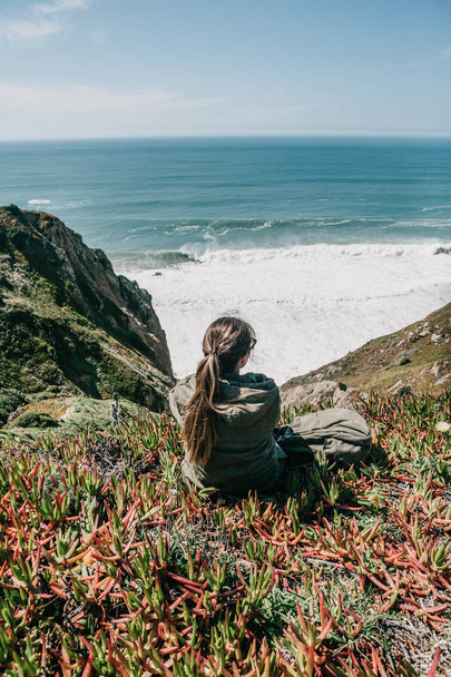 Ein Touristenmädchen mit Rucksack genießt an einem Frühlingstag einen schönen Blick auf den Atlantik - Foto, Bild