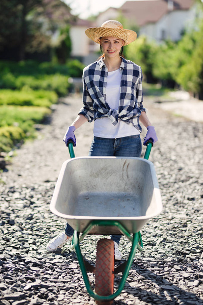 Portrait of cute gardener girl with wheelbarrow working in garden market - Fotó, kép