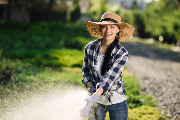 Beautiful young gardener woman watering garden in hot summer day - Photo, Image