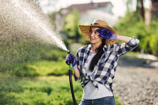 Beautiful young gardener woman watering garden in hot summer day - Fotó, kép