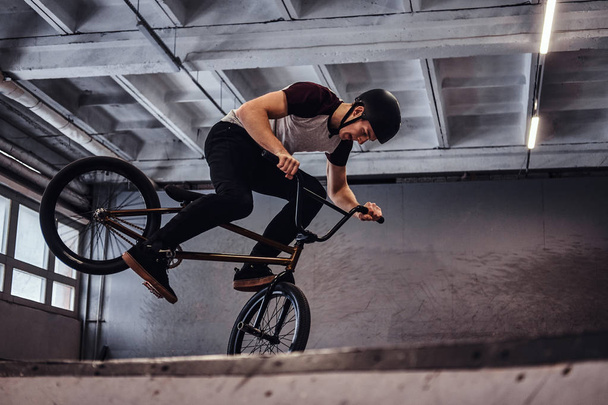Young man with BMX performing tricks in skatepark indoors - Foto, Bild