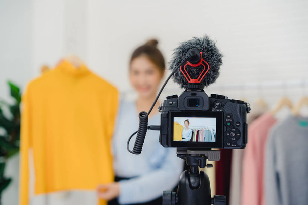 Azjatycka moda blogger kobiet online influencer gospodarstwa torby na zakupy i dużo ubrań na wieszak na ubrania dla nagrywania nowej mody transmisji wideo na żywo wideo do sieci społecznej przez internet w domu. - Zdjęcie, obraz