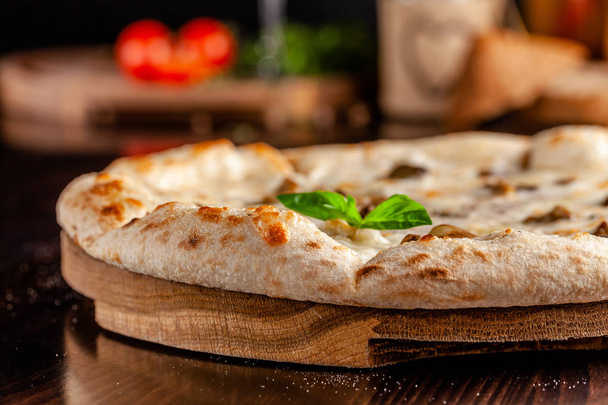 The concept of Italian cuisine. Thin cheese pizza with mushrooms, with large sides of Semola flour. A string of red wine on the table. Serving dishes in the restaurant - Φωτογραφία, εικόνα