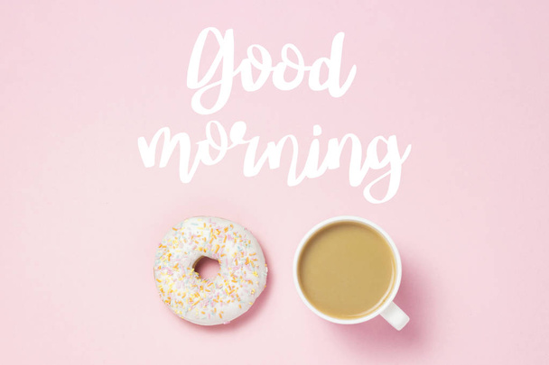 Cup met koffie of thee, vers smakelijke zoete donut op een roze achtergrond. Toegevoegde tekst Goedemorgen. Concept van de bakkerij, vers gebak, heerlijk ontbijt, fastfood, koffie shop. Plat lag, top uitzicht - Foto, afbeelding