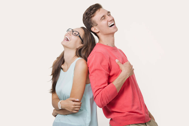Happy young lovely couple standing back to back and laughing over white background. Friendship and relationships - Φωτογραφία, εικόνα