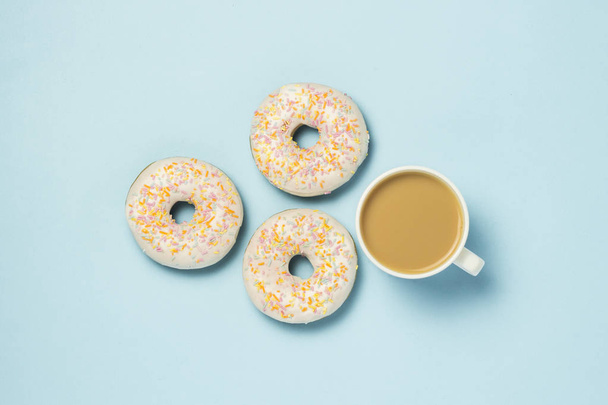 Witte kopje, koffie of thee met melk en verse lekkere donuts op een blauwe achtergrond. Concept van de bakkerij, vers gebak, heerlijk ontbijt, fastfood. Plat lag, top uitzicht - Foto, afbeelding