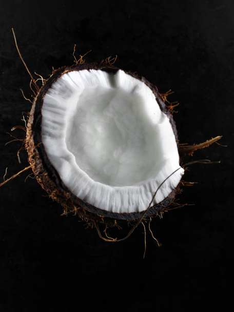 one half of chopped fresh coconut on a dark background - Foto, Imagem