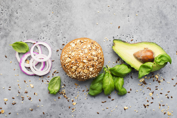 Ingredients for making healthy vegetarian avocado burger with basil, red onion, avocado on cereal buns. Gray light background. Top view, space. - Photo, image