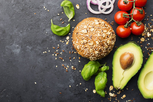 Ingredients of burger with avocado. Vegetable burger made from wholegrain bun, avocado, sweet onions, cherry tomatoes, basil on a dark background. Top view, space. - Foto, Imagem