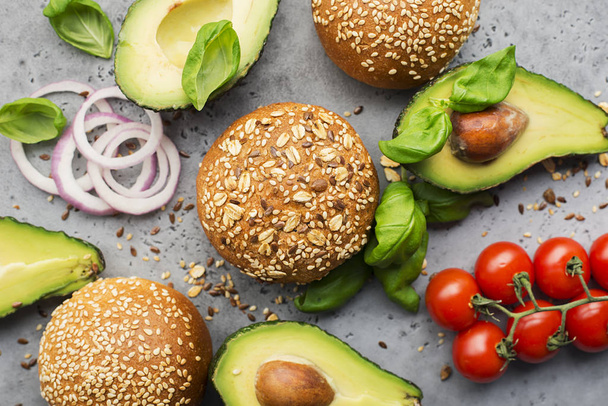 Healthy food. Veggie burger ingredients cereal buns, avocado, cherry tomatoes, basil, sweet onions on a light gray background. Top view, space. - Φωτογραφία, εικόνα