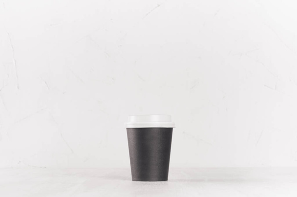 Coffee mockup - small blank black paper cup with white cap on white wood table, coffee shop interior. Modern elegant concept for branding identity, advertising, design. - Foto, Imagem