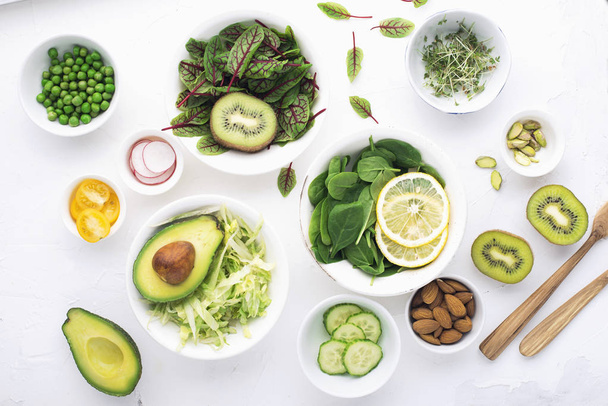 Green ingredients for spring detox salads: spinach, sorrel with red veins, cucumbers, radishes, iceberg lettuce, green peas, avocados, lemon, microgreen, yellow tomatoes on a white background with - Photo, Image