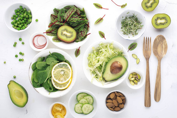 Green ingredients for spring detox salads: spinach, sorrel with red veins, cucumbers, radishes, iceberg lettuce, green peas, avocados, lemon, microgreen, yellow tomatoes on a white background with - Foto, Bild