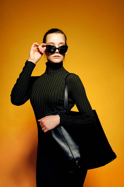Black friday sale concept. Shopping woman holding black leather bag isolated on yellow background - Valokuva, kuva