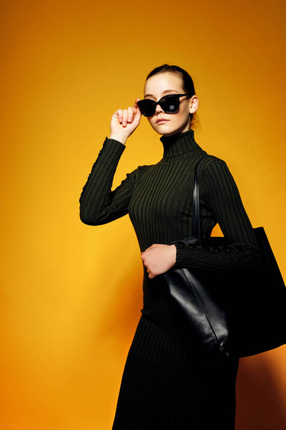 Black friday sale concept. Shopping woman holding black leather bag isolated on yellow background - Fotografie, Obrázek