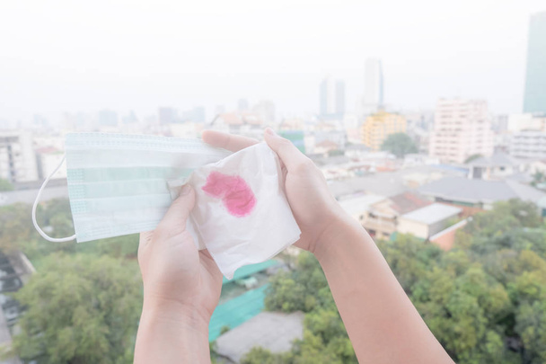 Žena rukou nebo ženské ruce držící ochrannou masku a ubrousek s krví kvůli znečištění ovzduší ve městě mají částice nebo Pm 2,5 s městem budování pozadí - Fotografie, Obrázek
