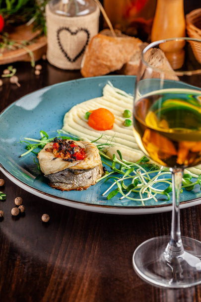 The concept of Italian cuisine. Baked Seabass Fish with Vegetables and Mashed Potatoes. A glass of white wine on the table. Servovika dishes in the restaurant. copy space - Foto, afbeelding