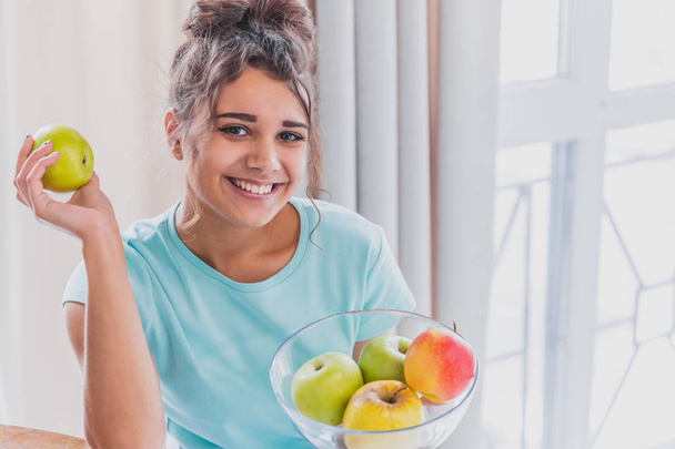 Young Happy Woman Refreshing with Cup of Coffee, Snacks and Fresh Fruit at the Kitchen Table in the Early Morning. - Foto, Imagem