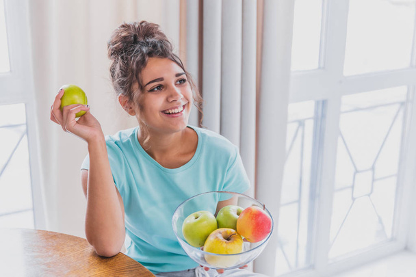 Young Happy Woman Refreshing with Cup of Coffee, Snacks and Fresh Fruit at the Kitchen Table in the Early Morning. - Foto, Bild