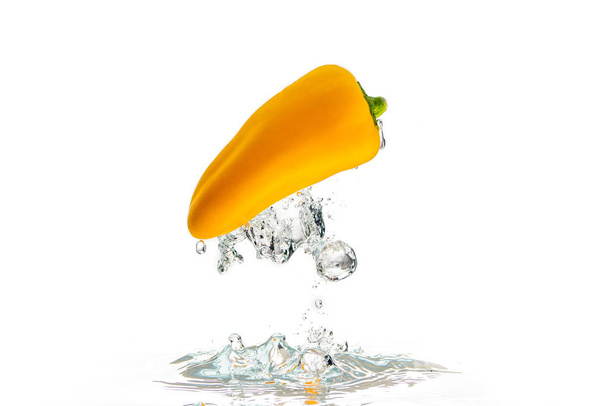 Gelber Paprika fällt mit einem Spritzer unter Wasser. mit vielen Luftblasen auf dem Kopf - Foto, Bild
