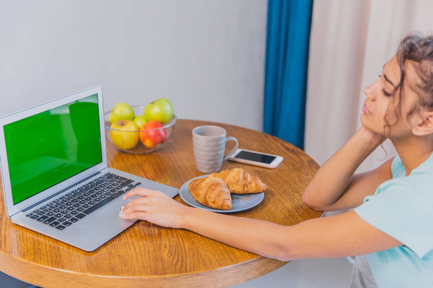 Beautiful young woman at home in the kitchen with laptop and mobile works via Internet.Green screen - Φωτογραφία, εικόνα