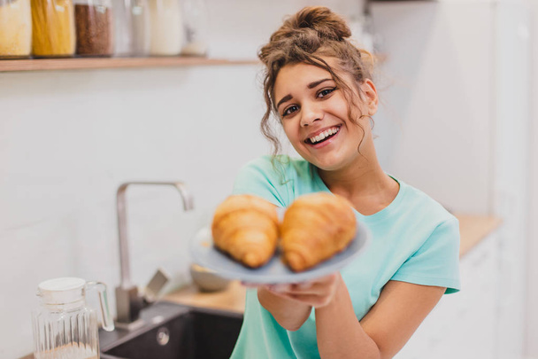 Young girl in the morning in the kitchen. It looks like a hand, a womans hand holds croissants on a plate. - Фото, изображение