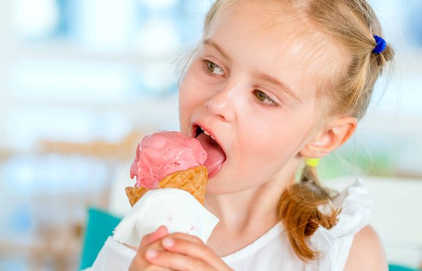 Little blond girl eating pink ice cream - Zdjęcie, obraz