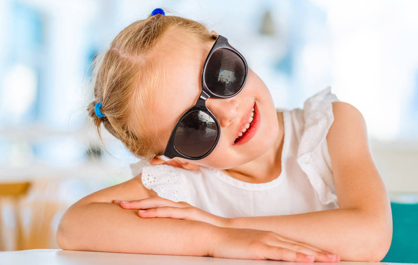 Little smiling blond girl in black sunglasses - Фото, изображение