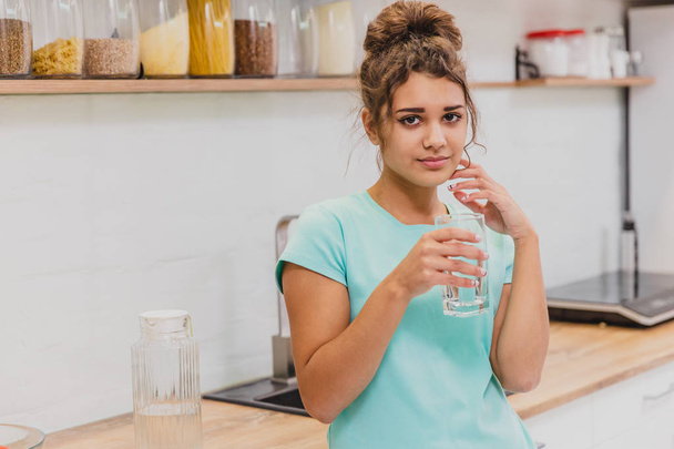 Happy beautiful young woman drinking water. Smiling caucasian female model holding transparent glass in her hand. - Foto, imagen