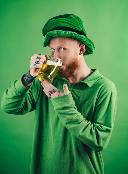 Lucky charms on green background. Leprechauns hat. Man on green background celebrate St Patricks Day. Portrait of excited man holding glass of beer on St Patricks day isolated on green. - Fotoğraf, Görsel