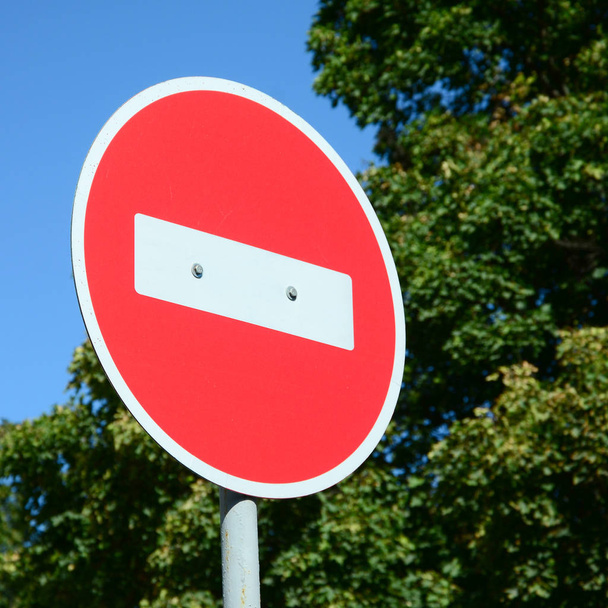 Un letrero rojo circular con una barra blanca que indica NO ENTRADA en un poste de metal gris contra un árbol verde y un cielo azul claro
 - Foto, imagen
