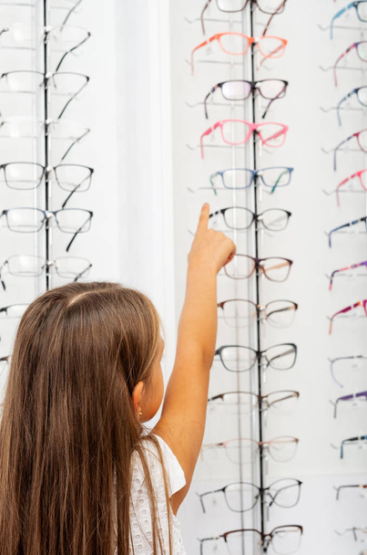 Little blond girl pointing on the glasses on the showcase - Photo, Image