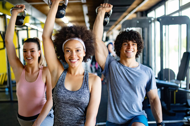 Group of young happy people doing exercises in gym - Photo, image