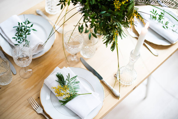 Beautiful springtime table setting with green leaves and mimosa branches, bright white table dinner decoration - Foto, immagini