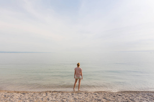 Ευτυχισμένο ξέγνοιαστο γυναίκα απολαμβάνοντας το ηλιοβασίλεμα με τα πόδια στην παραλία Pabbled λευκό. - Φωτογραφία, εικόνα