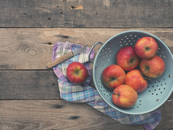 Delicious organic apples in an old used colander on a rustic wooden table, flat tone vintage style with view from above - Photo, Image