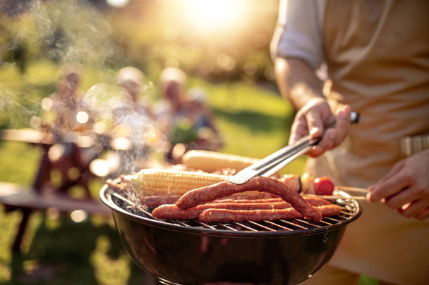 Дозвілля, їжа, люди та свята концептуальний чоловік готує м'ясо на грилі для барбекю для своєї сім'ї на літній відкритій вечірці
. - Фото, зображення