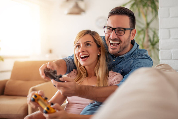 Χαρούμενο ζευγάρι παίζει βιντεοπαιχνίδια στο διαμέρισμά τους. - Φωτογραφία, εικόνα