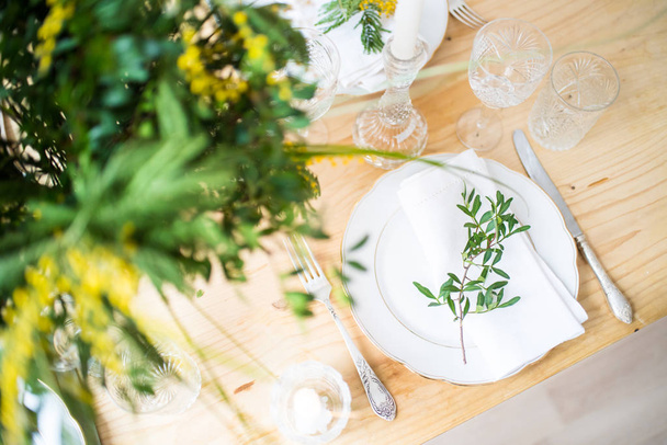 Beautiful springtime table setting with green leaves and mimosa branches, bright white table dinner decoration - Photo, Image