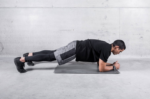 Side view of athlete in sportswear doing plank exercise for abdomen muscles  - Foto, Imagen