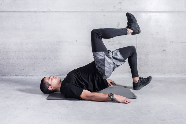 Side view of sportive man lying on concrete floor and doing hip raises  - Photo, image