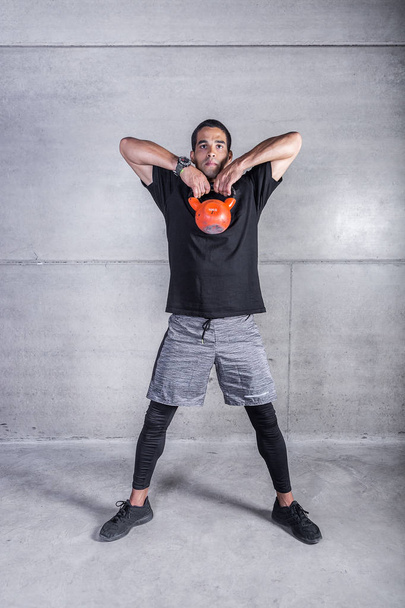 Strong personal trainer working out with kettlebell standing on gray concrete backdrop  - Foto, Bild