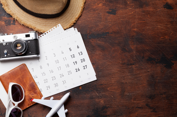 Concepto de fondo de vacaciones de viaje con calendario, sombrero de sol, cámara, pasaporte y juguete de avión sobre fondo de madera. Vista superior con espacio de copia. Puesta plana
 - Foto, Imagen