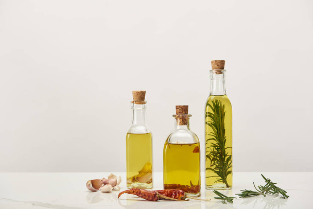 garrafas de óleo aromatizado com alecrim e várias especiarias na superfície branca
 - Foto, Imagem