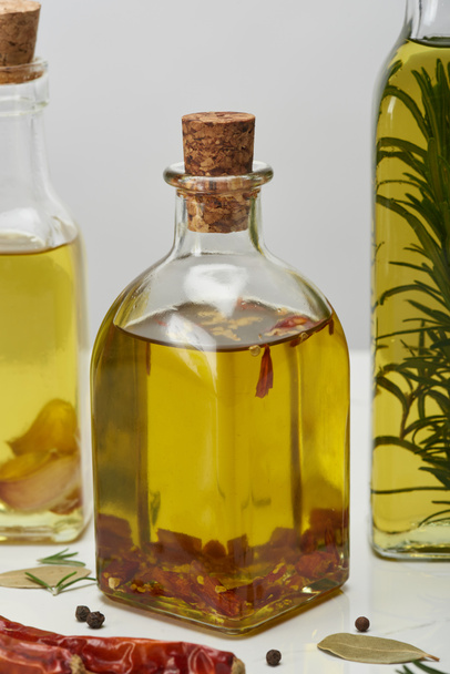 various bottles of oil flavored with different spices and rosemary on white surface - Fotografie, Obrázek